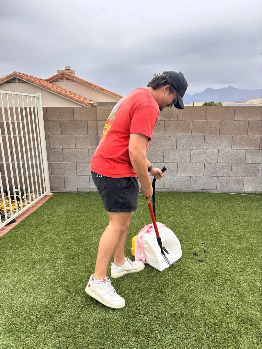A Scoop Doggy Logs worker scooping dog waste from a turf yard
